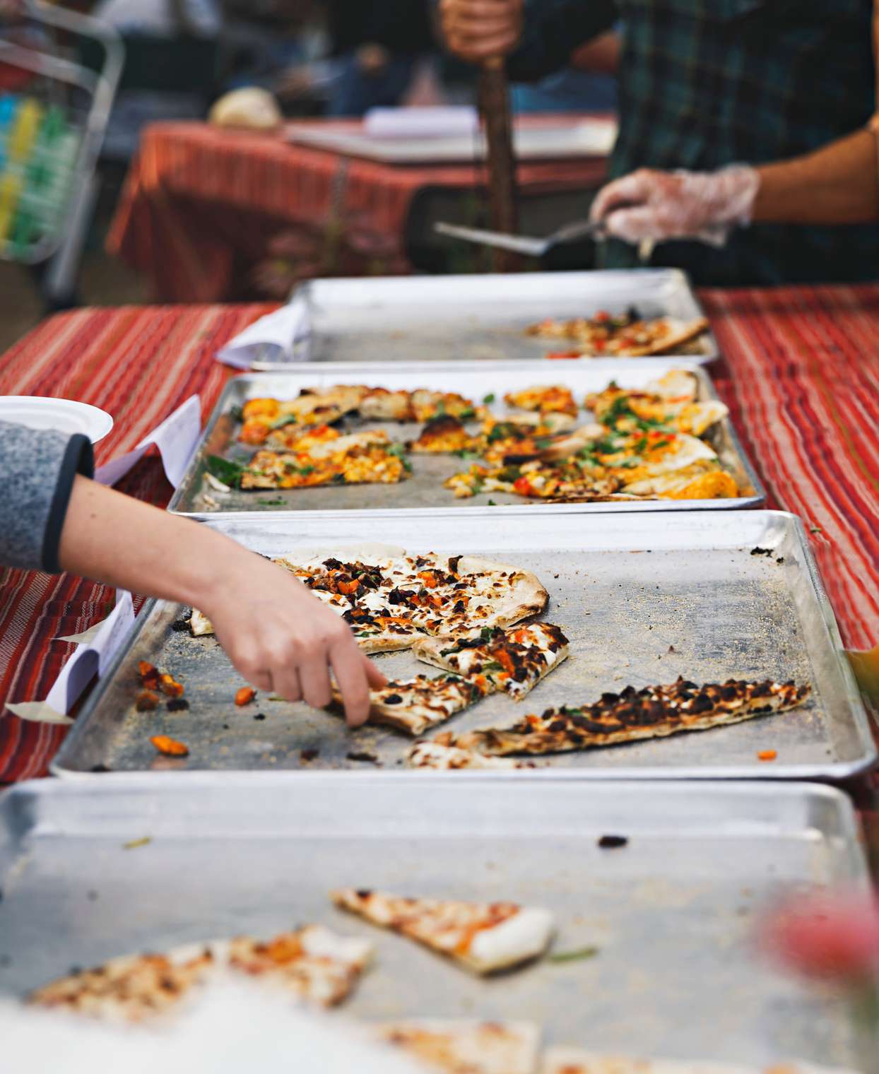 customers taking pizza slices from sheet pan